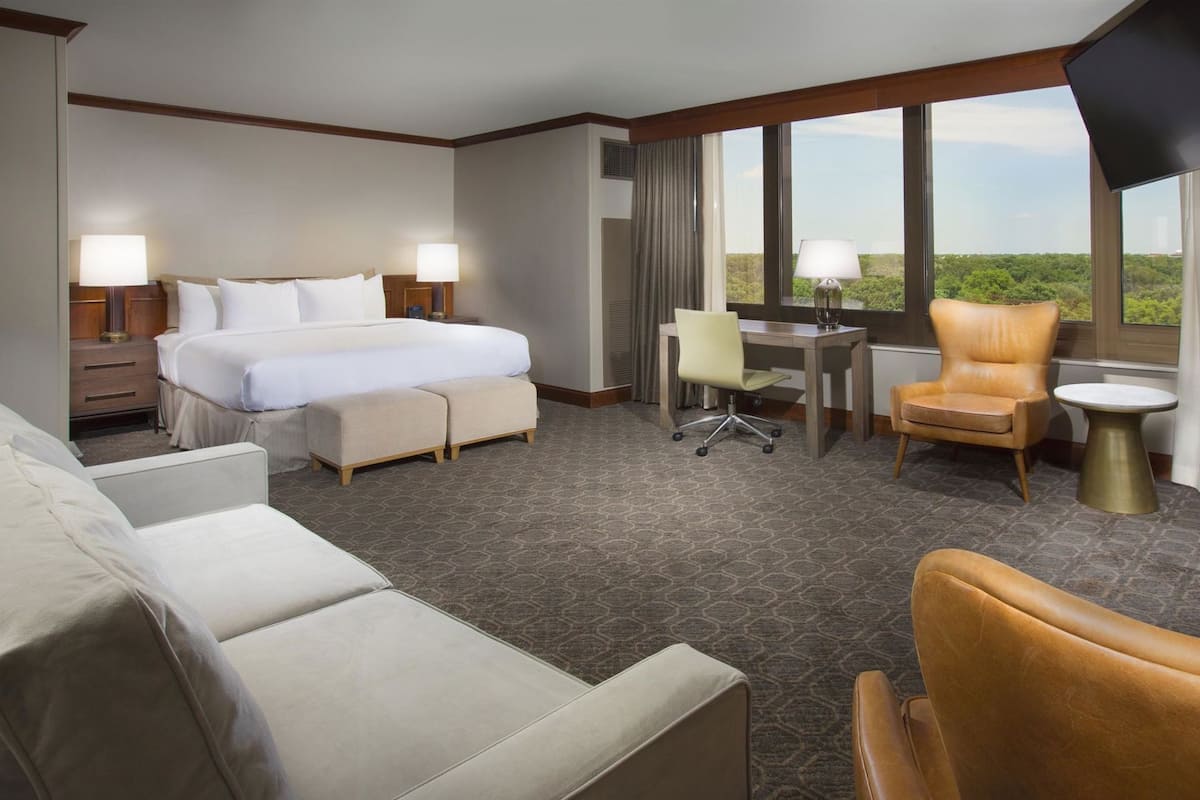 A hotel room with a bed, desk, two chairs, a sofa, and a TV.
