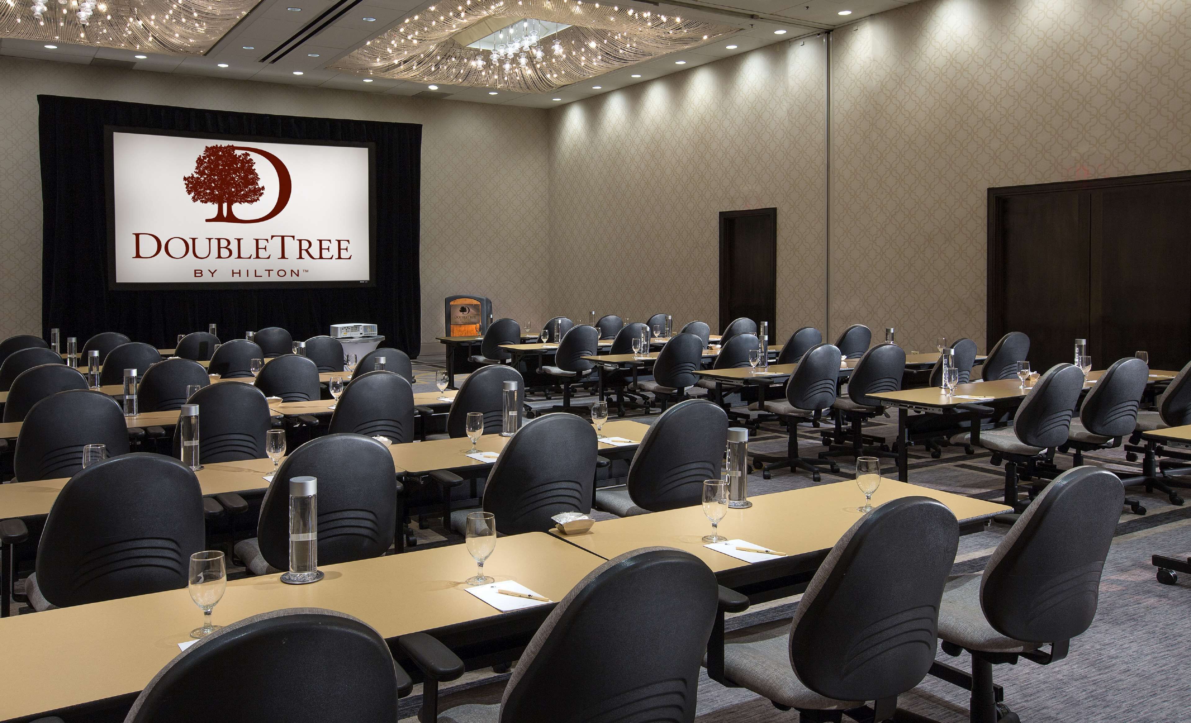 A conference room with multiple tables and chairs, a large screen displaying the DoubleTree logo, and a chandelier.