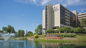A modern hotel building with a sign reading "DOUBLETREE BY HILTON" in front of a landscaped area with a pond and fountain.