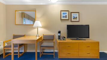 A hotel room with a wooden desk, two chairs, a television, a coffee maker, and a dresser.