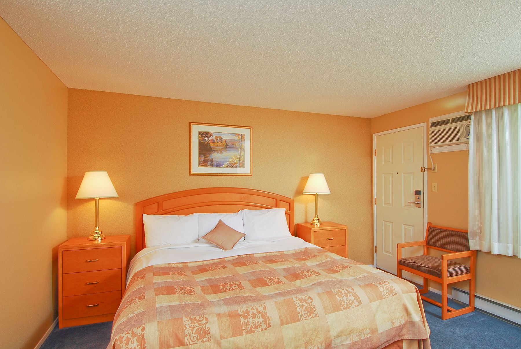 A hotel room with a bed, two bedside lamps, a chair, a door, and a picture on the wall.