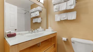 Un baño con lavamanos blanco, espejo y toallero.