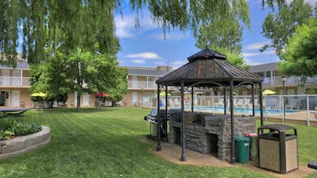 A gazebo with a stone fireplace, a pool, and a well-maintained lawn.