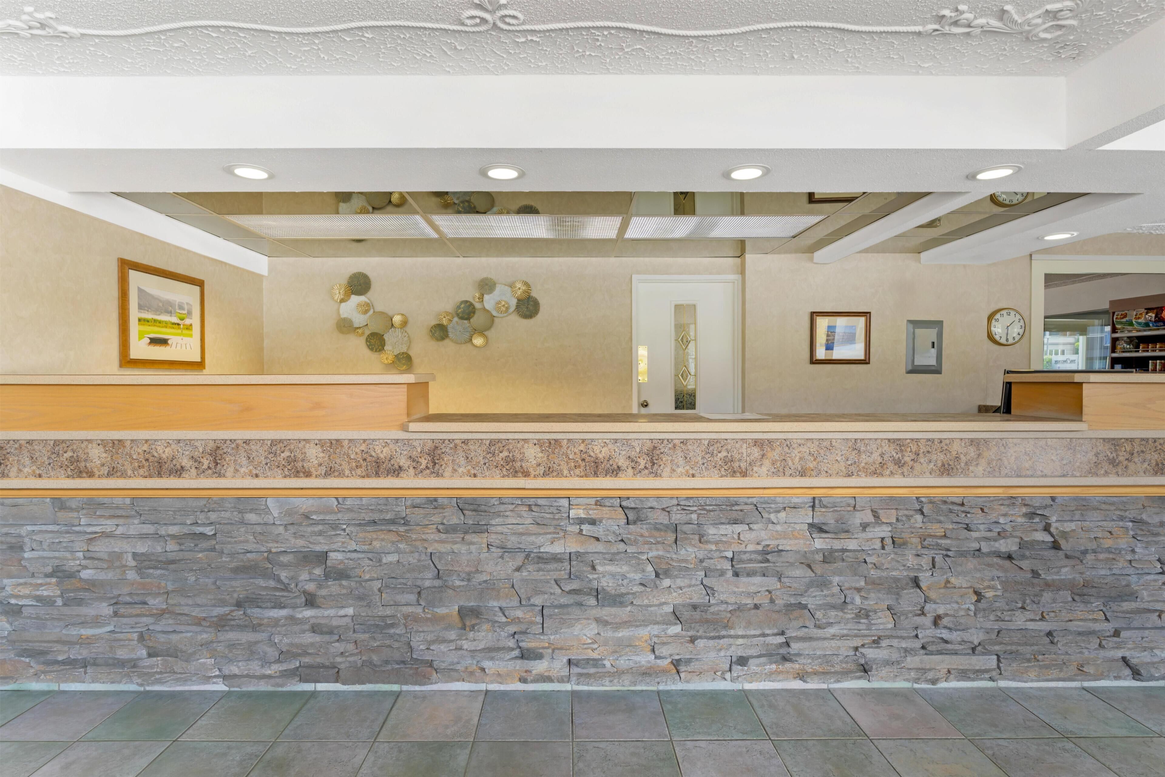 A reception area with a stone wall, a wooden reception desk, a framed picture, and a wall-mounted clock.