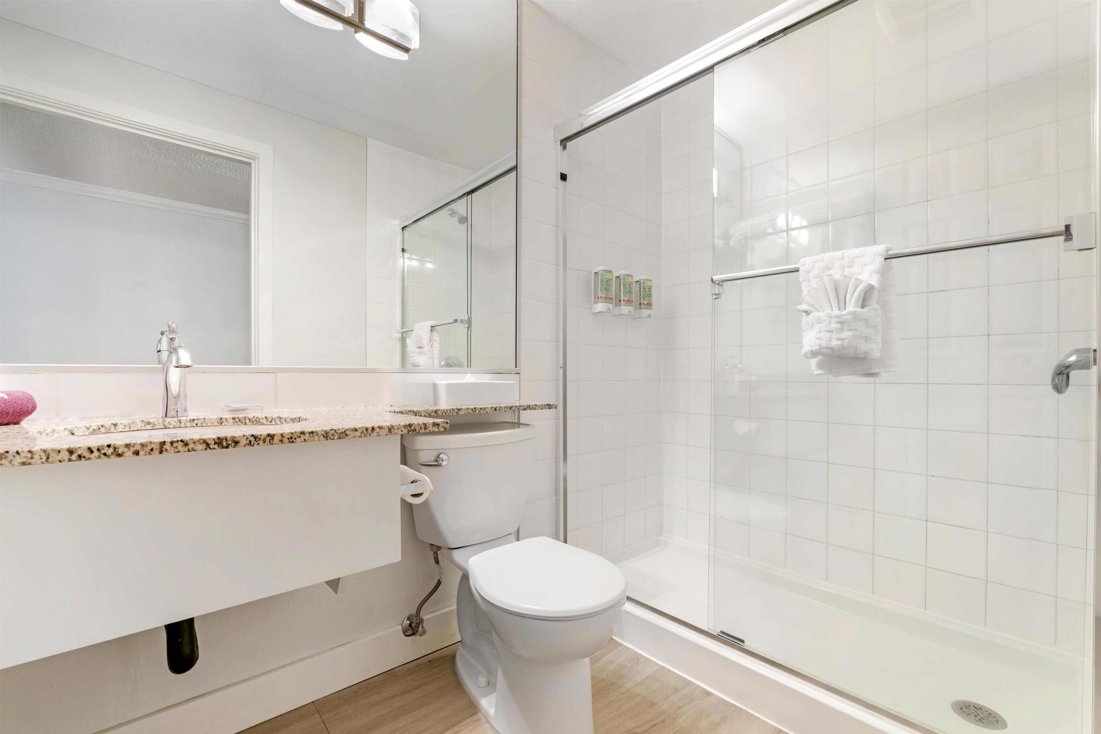 Un baño moderno con cabina de ducha de vidrio, inodoro blanco y tocador con encimera de granito.