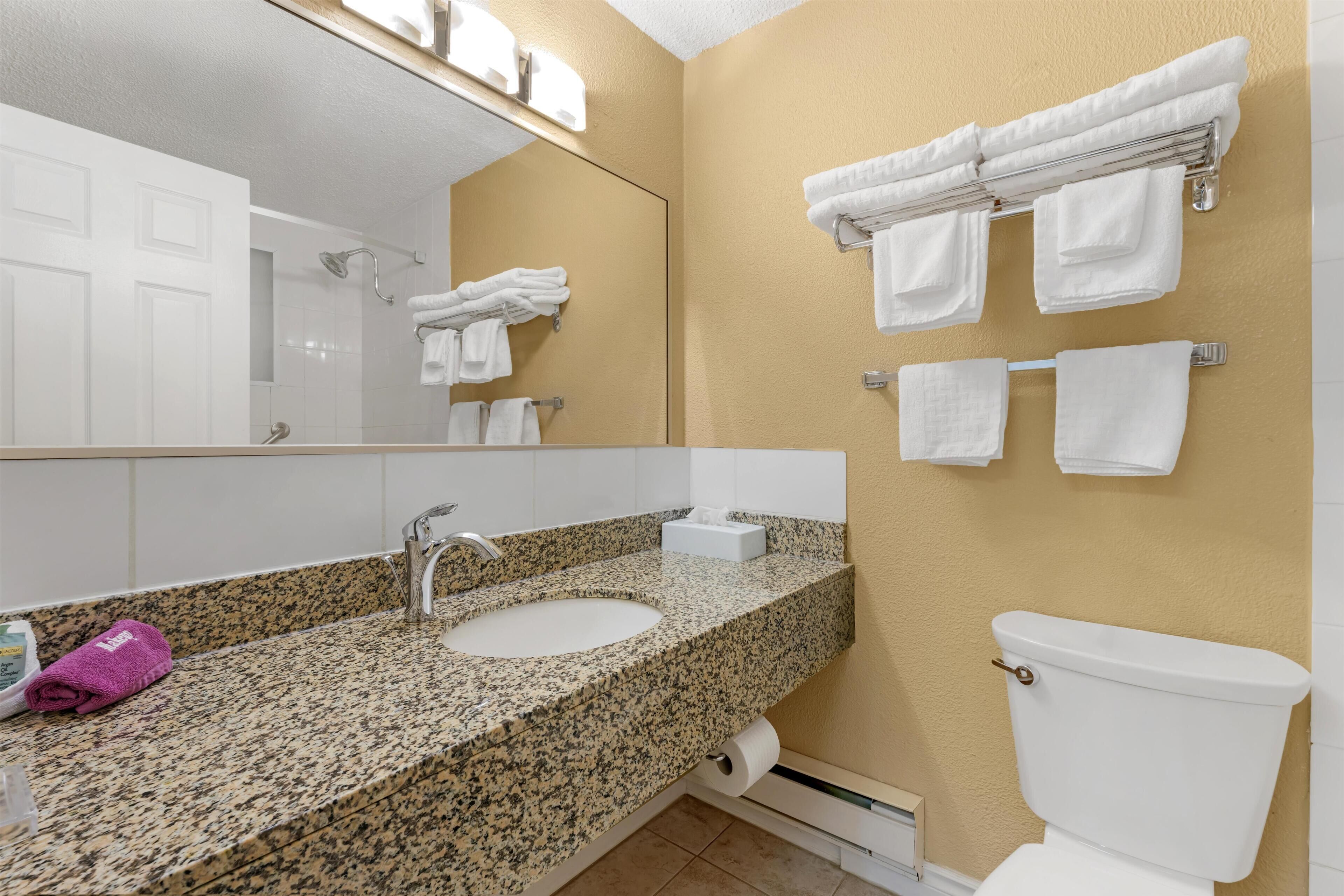 A bathroom with a granite countertop, a sink, a toilet, and towels on the wall.
