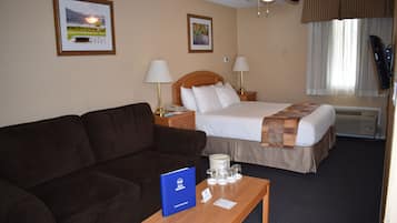 Habitación de hotel con cama, sofá, mesita de noche con lámpara, ventilador de techo y cuadros en la pared.