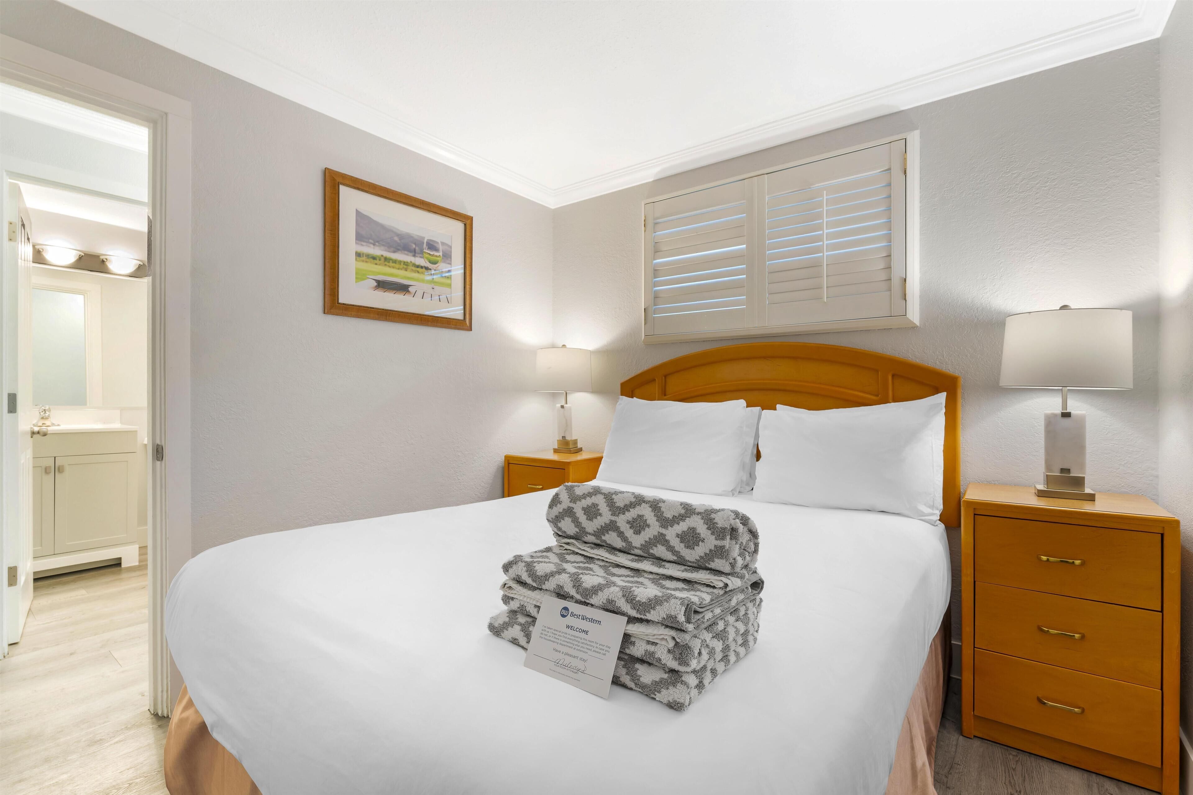 A neatly made bed with a folded blanket, a bedside lamp, a nightstand, and a framed picture on the wall.