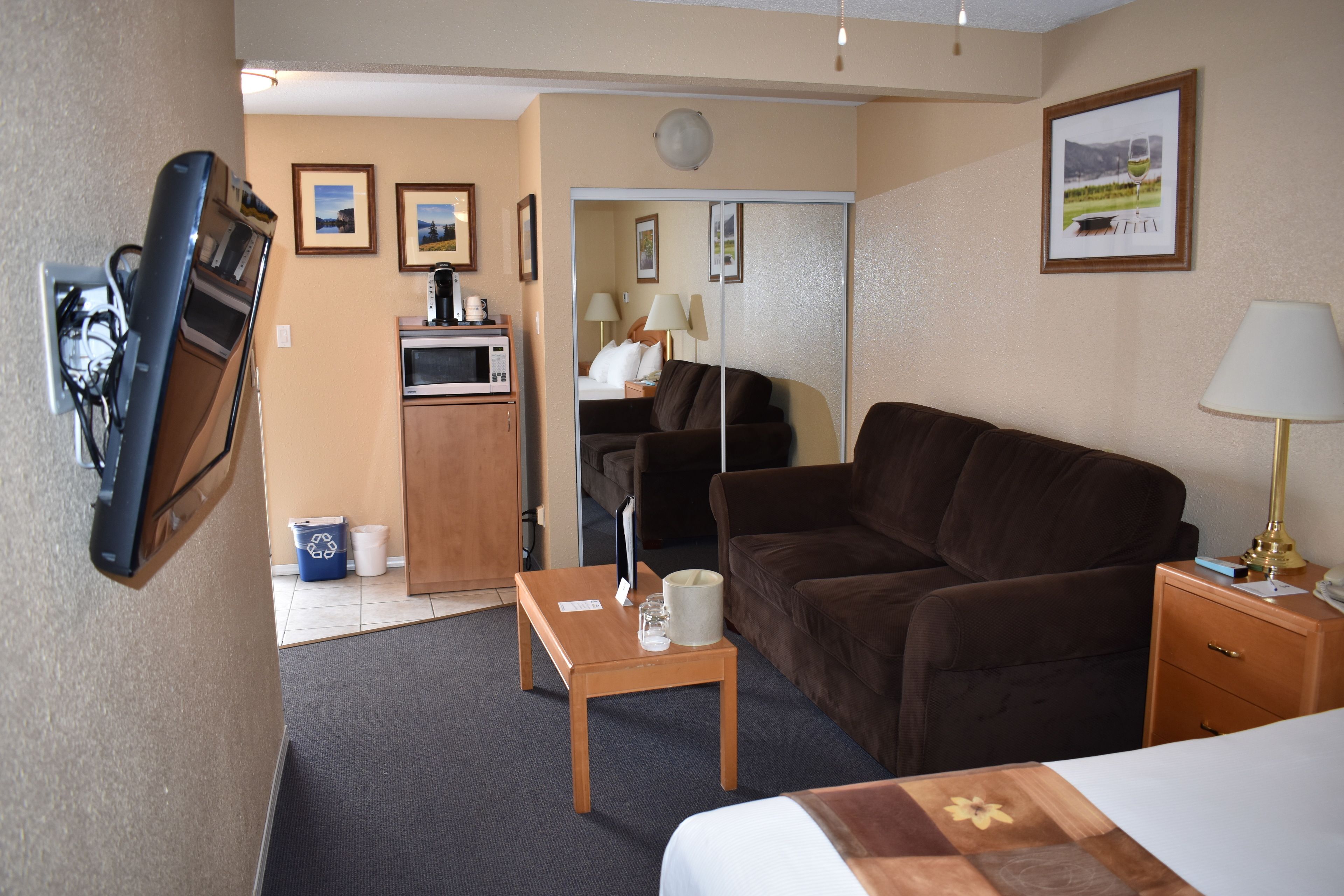 A hotel room with a bed, a brown sofa, a wooden table, a lamp, a TV, and a microwave.