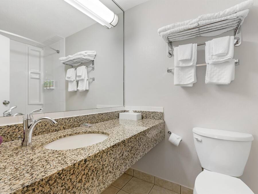 Un baño con encimera de granito, un lavamanos, un espejo, un inodoro y toalleros.