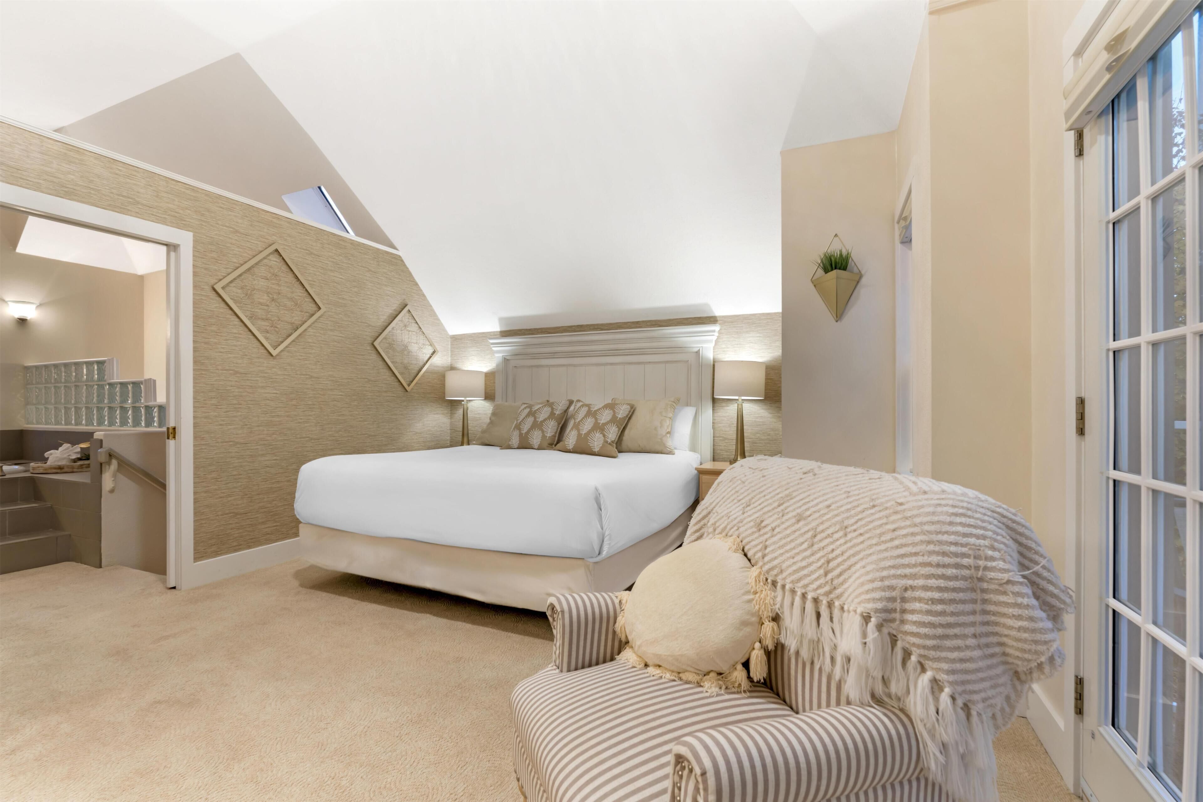 A bedroom with a bed, a chair, a nightstand, a window, and a door.
