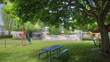 Relax in our serene outdoor space, featuring a lawn with a picnic table and benches, a playground for kids, and shaded by mature trees.