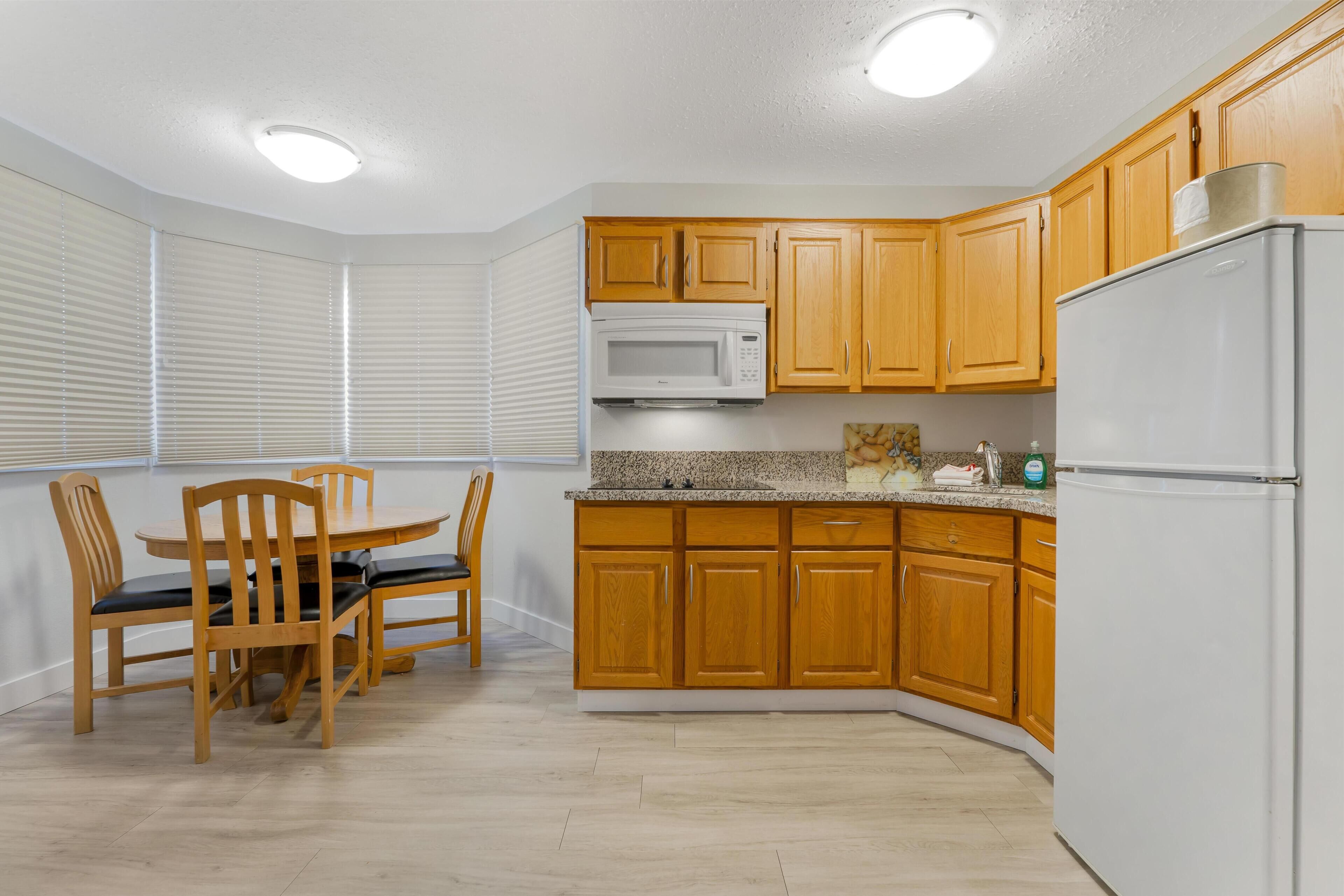 A kitchen with wooden cabinets, a microwave, a refrigerator, and a dining table with chairs.