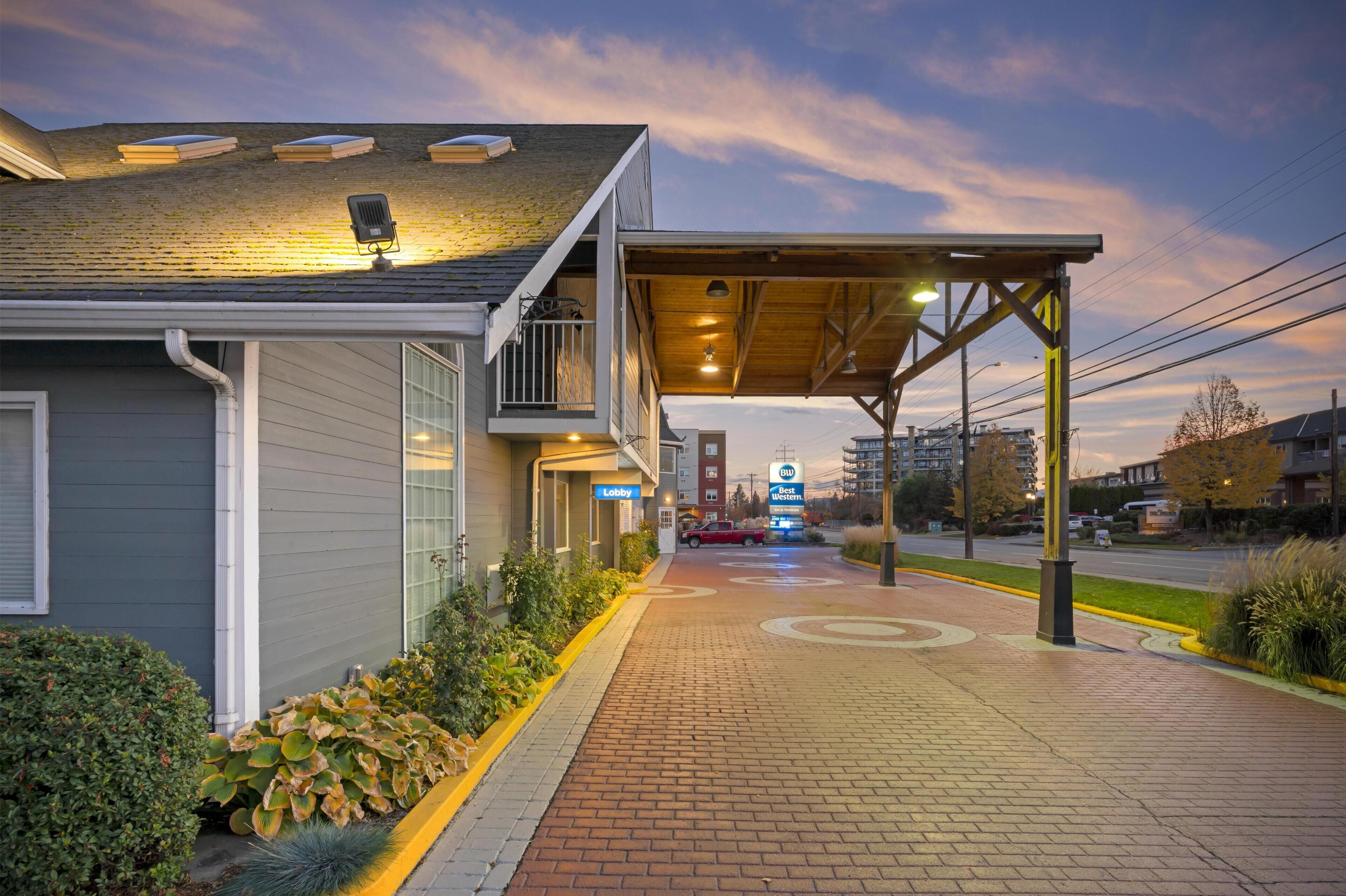 A hotel entrance with a covered walkway, a 'Lobby' sign, and a 'Best Western' sign in the distance.