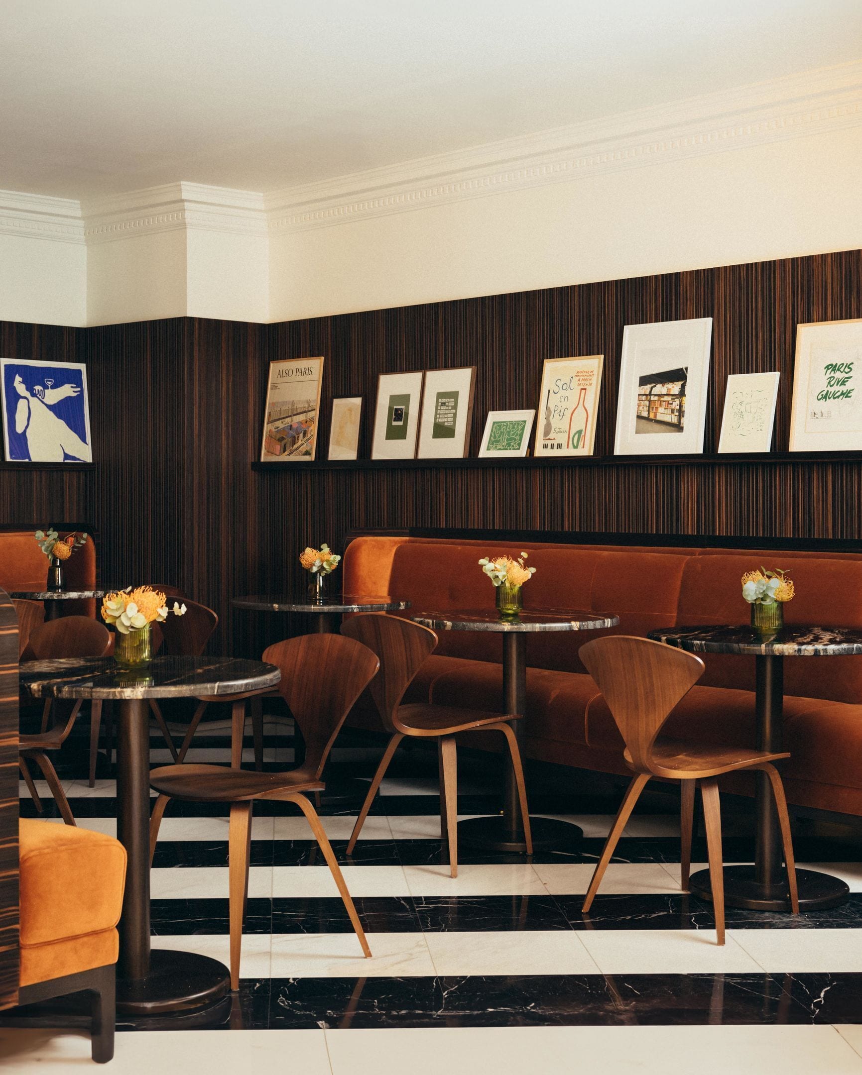 A restaurant interior with a black and white tiled floor, wooden chairs, a brown sofa, and framed pictures on the wall.