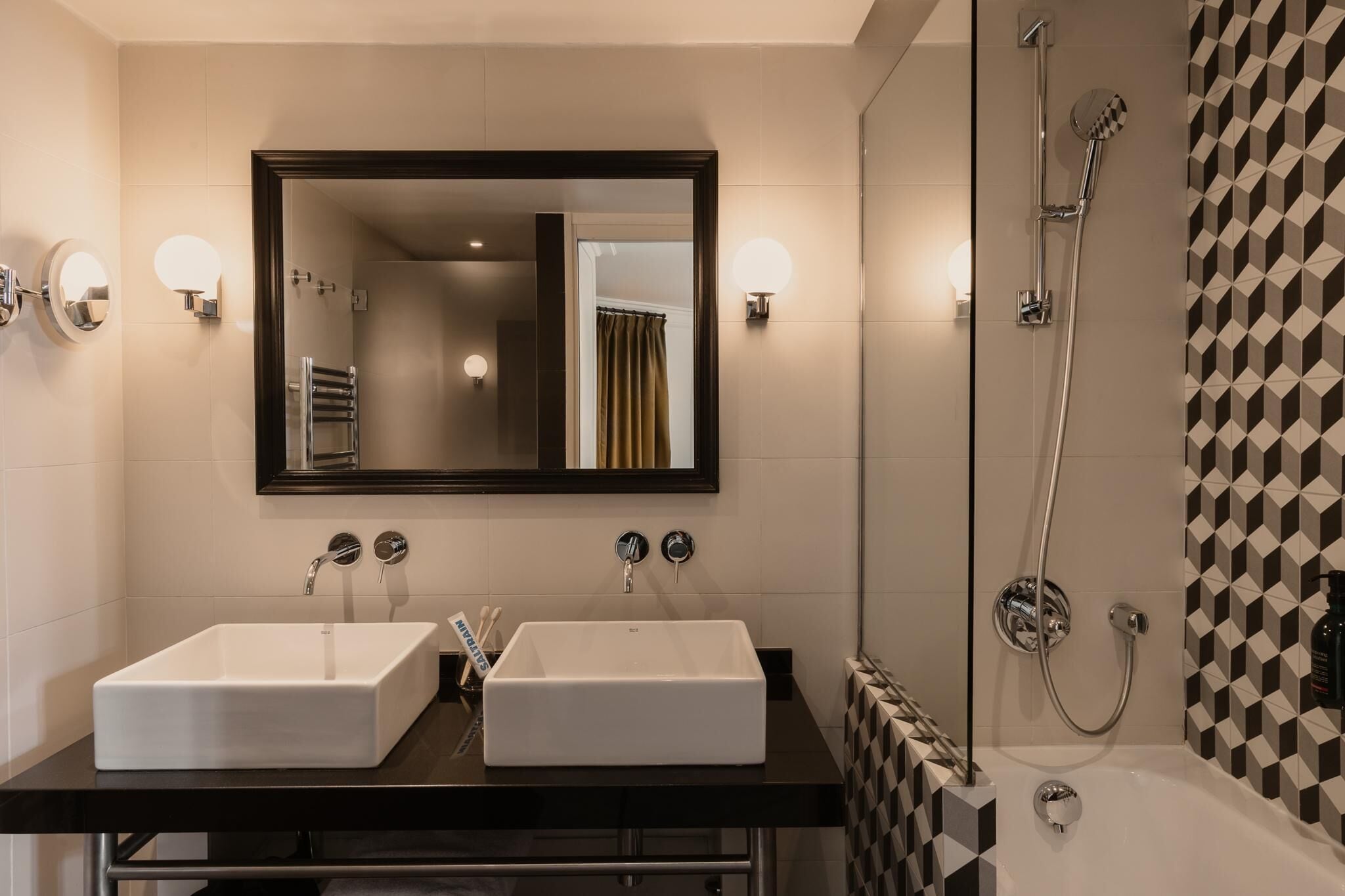 A modern bathroom with two sinks, a large mirror, and a shower.