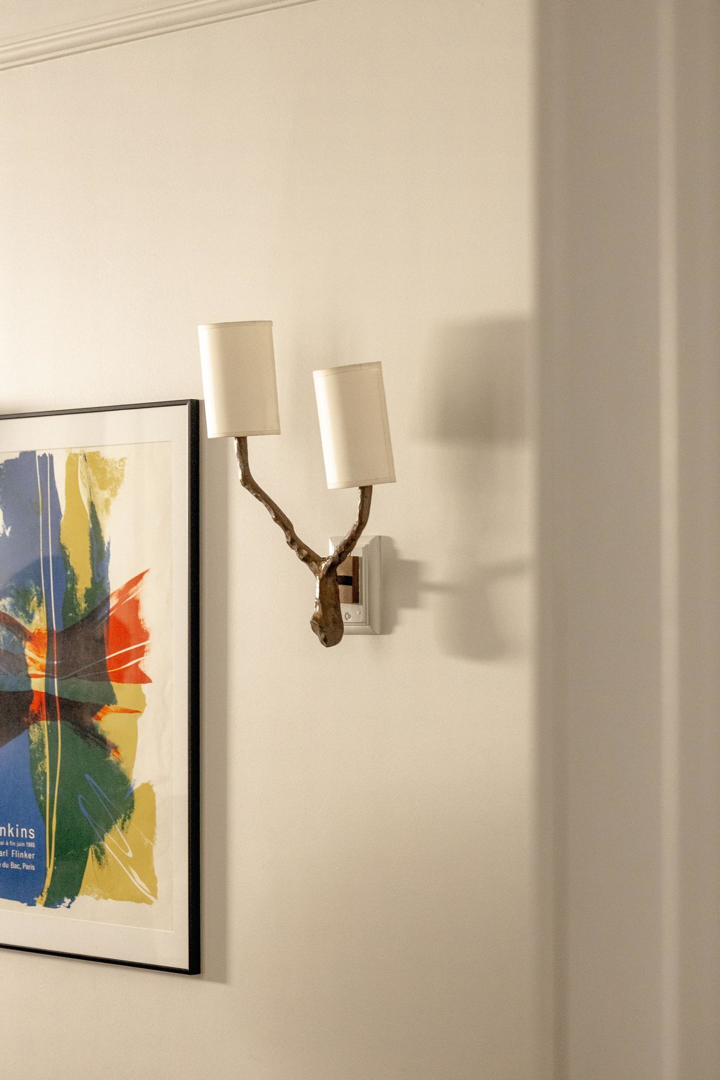 Una làmpada de paret amb disseny de branca, un quadre abstracte amb marc i una paret blanca.