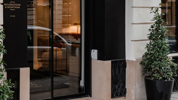 The exterior of the Bourgogne & Montana hotel with a black awning, large glass entrance, and potted plants.