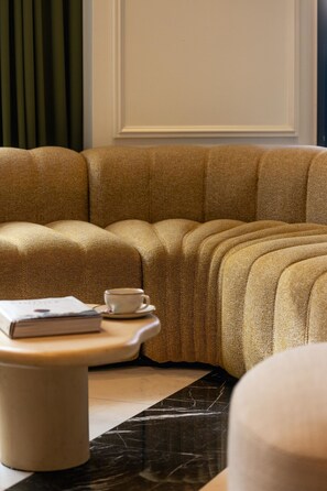 Ein Ecksofa mit Kissen, ein kleiner Tisch mit Tasse und Buch sowie ein Marmorboden.