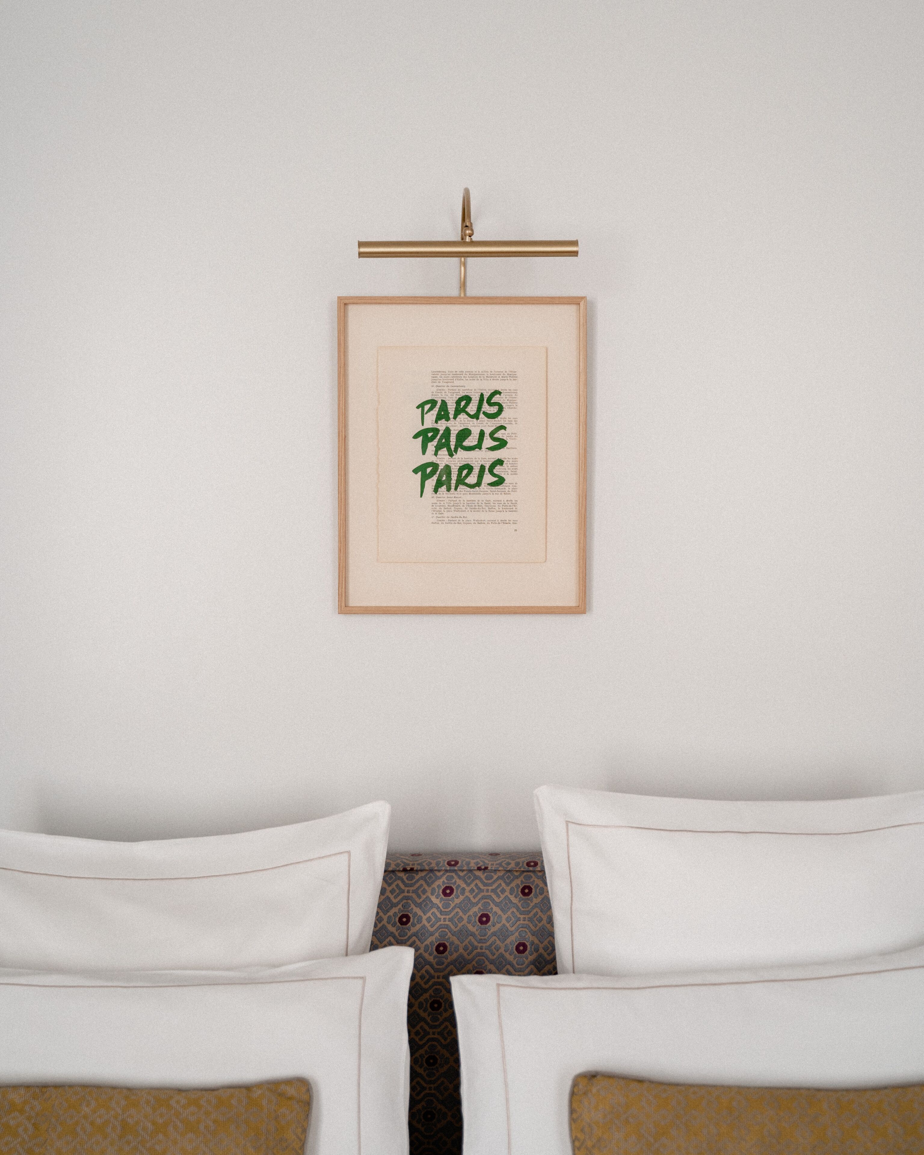 A framed text on a wall, two white chairs with patterned cushions, and a patterned pillow.