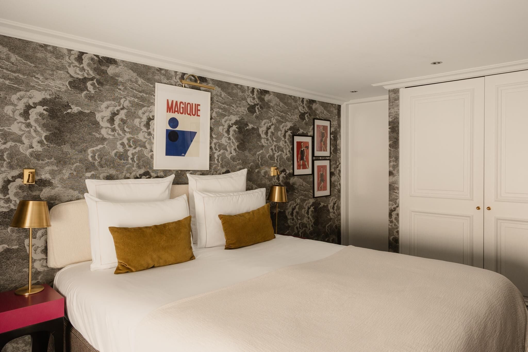 A bedroom with a large bed, two bedside tables, a nightstand, a wall-mounted artwork, and a wardrobe.