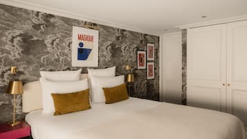 A bedroom with a large bed, two bedside tables, a nightstand, a wall-mounted artwork, and a wardrobe.