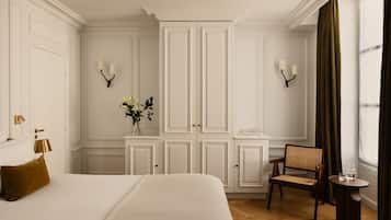 Une chambre d’hôtel avec un grand lit, une petite table, une chaise, un vase avec des fleurs et une armoire.