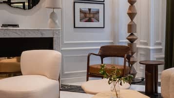 A modern living room with a fireplace, two framed artworks, a wooden chair, a round coffee table, and a decorative pillar.