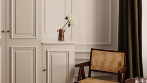 A room with a wooden floor, a wicker chair, a small table with a glass, and a wall-mounted light fixture.