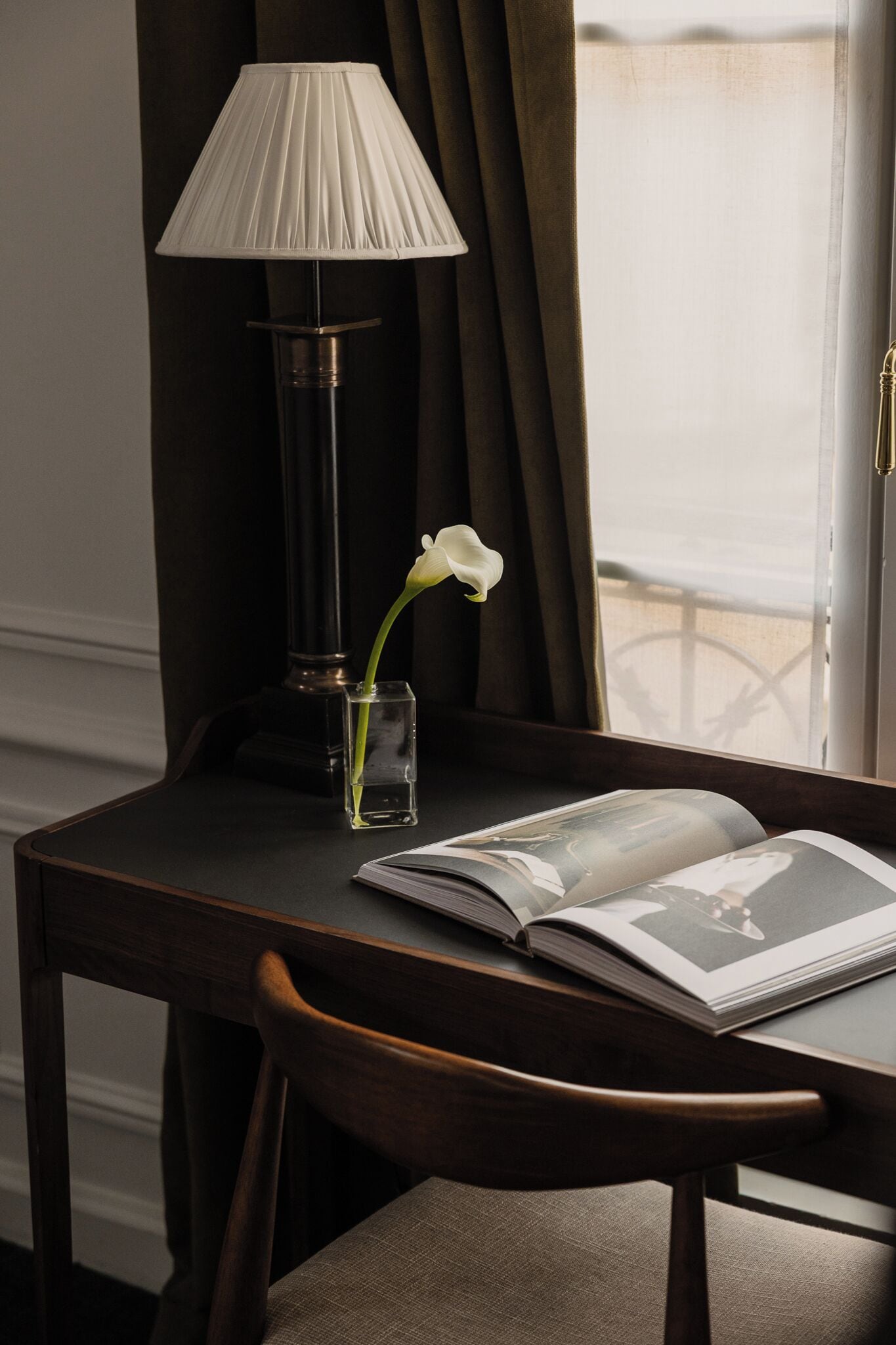 A wooden table with a lamp, a vase with a single flower, and an open magazine.