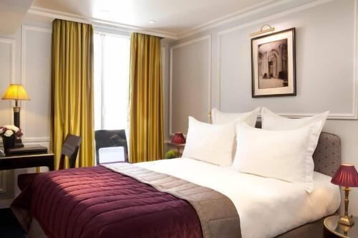 Une chambre d’hôtel avec un lit, un bureau, une chaise, une lampe et un tableau encadré au mur.