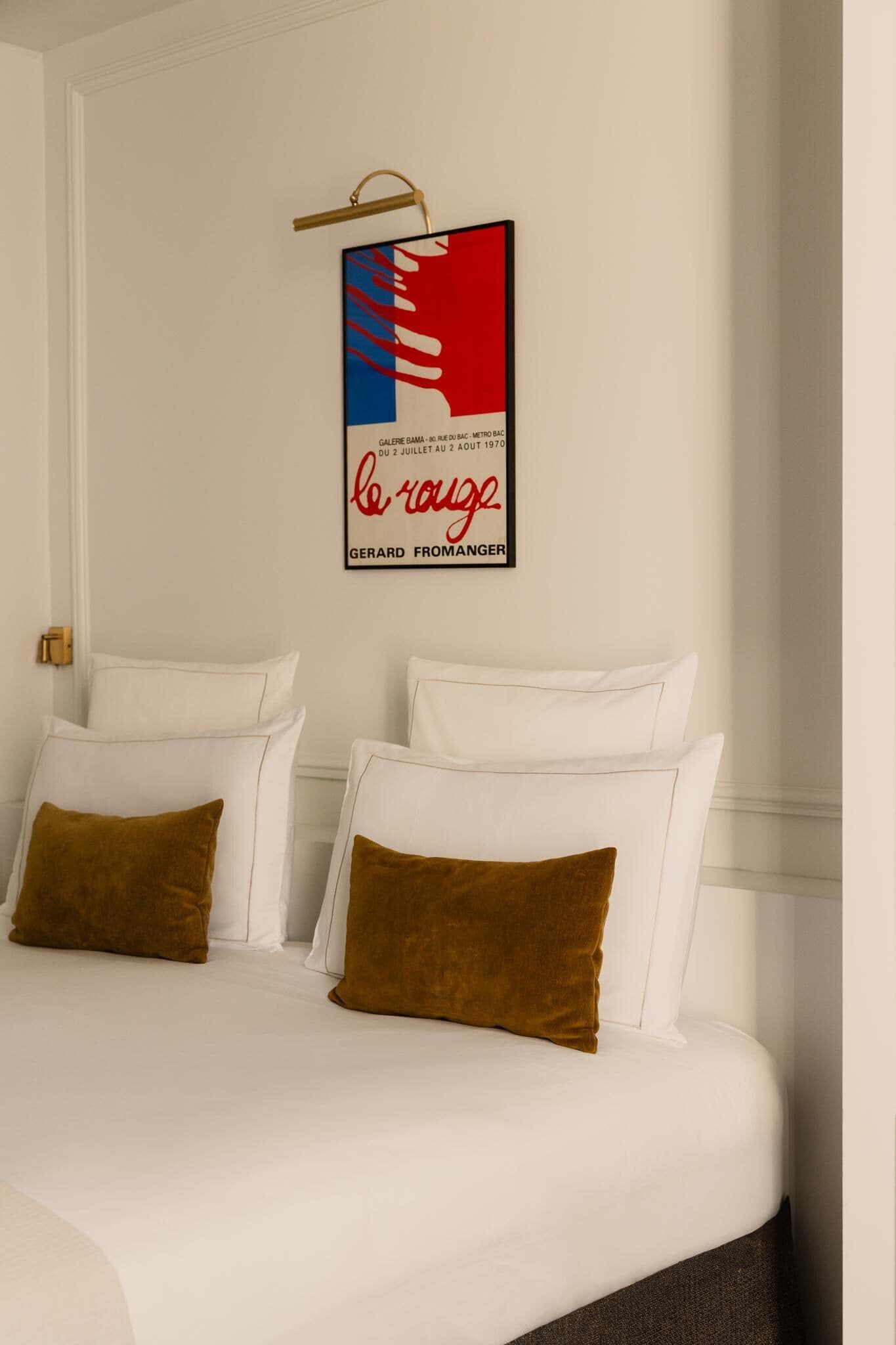 A hotel room with a bed, white bedding, and two brown pillows. A framed artwork hangs on the wall above the bed.