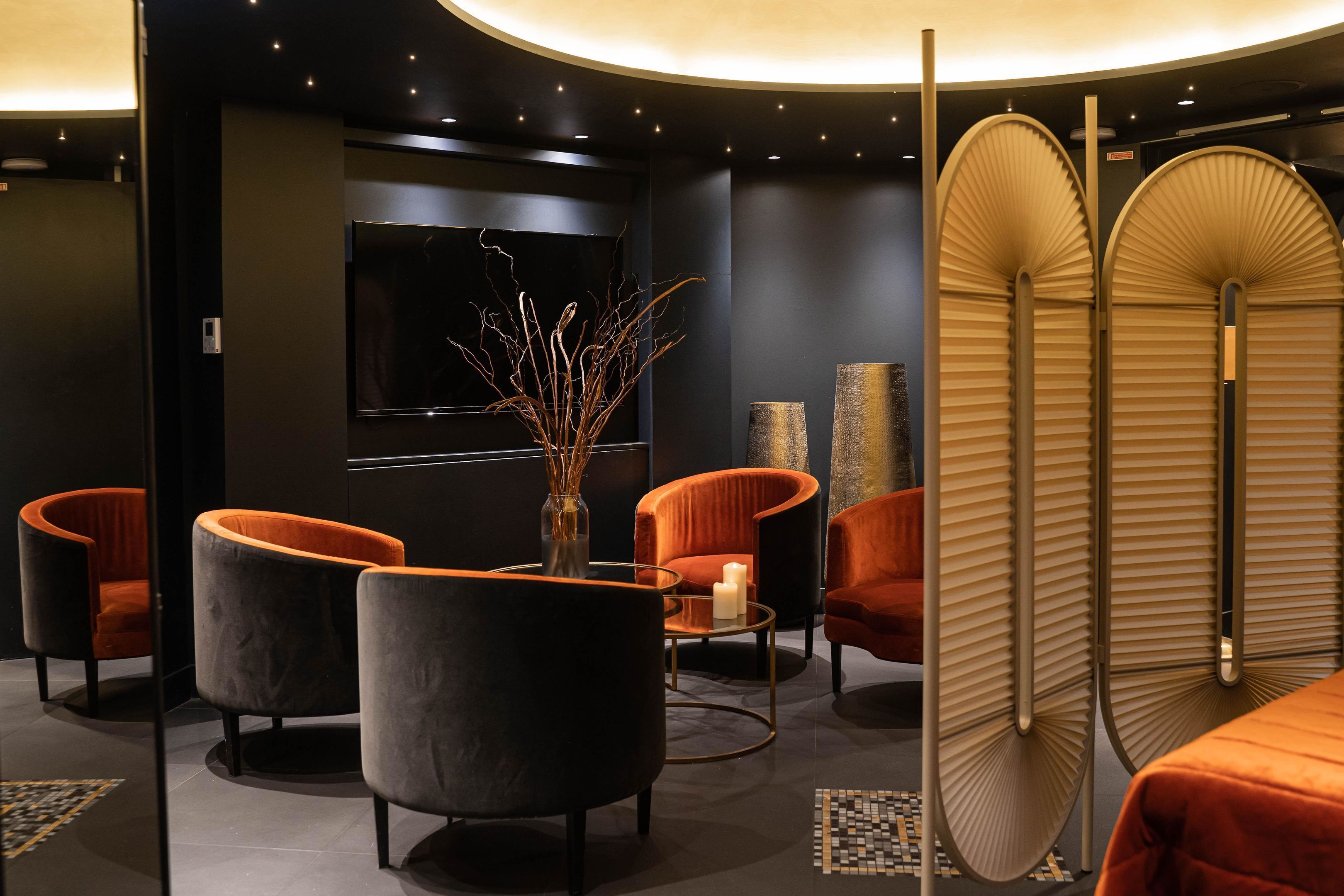 A modern lounge area with curved black and orange chairs, a glass coffee table, and a vase with branches.