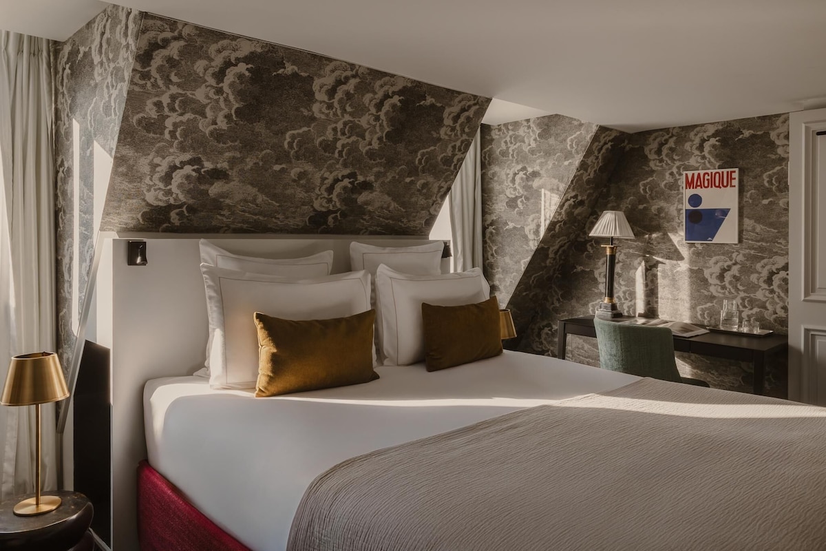 Une chambre d’hôtel avec un lit, un bureau, une lampe et un mur orné d’un motif de nuages.