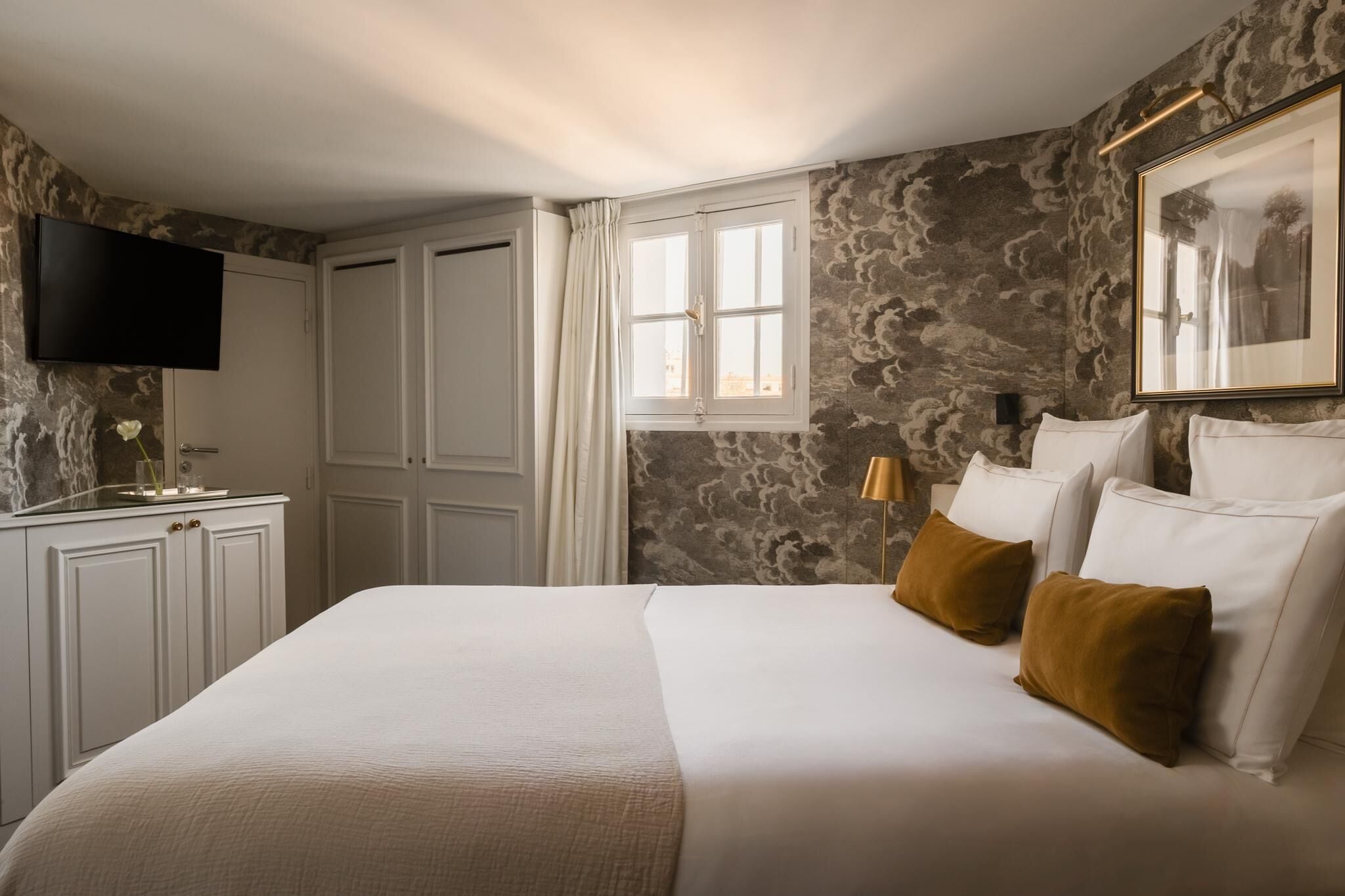 Une chambre d’hôtel avec un grand lit, un téléviseur à écran plat, une fenêtre avec des rideaux et un mur décoré d’un motif imitant la pierre.