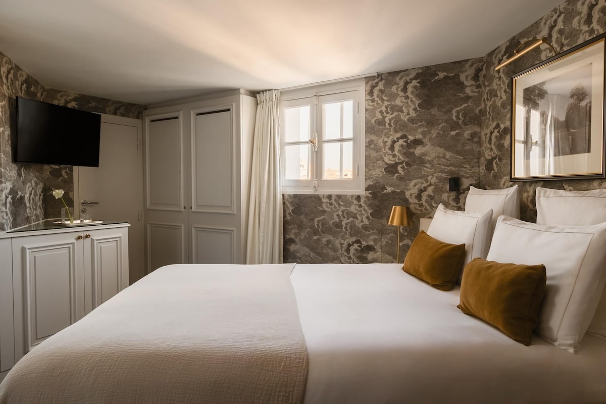 Une chambre d’hôtel avec un grand lit, un téléviseur à écran plat, une fenêtre avec des rideaux et un mur décoré d’un motif imitant la pierre.