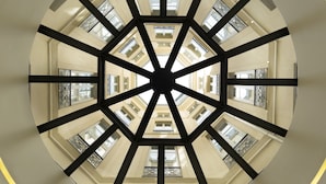 Une vue architecturale circulaire d’un bâtiment à plusieurs étages, mettant en valeur un espace central ouvert et une structure métallique géométrique.