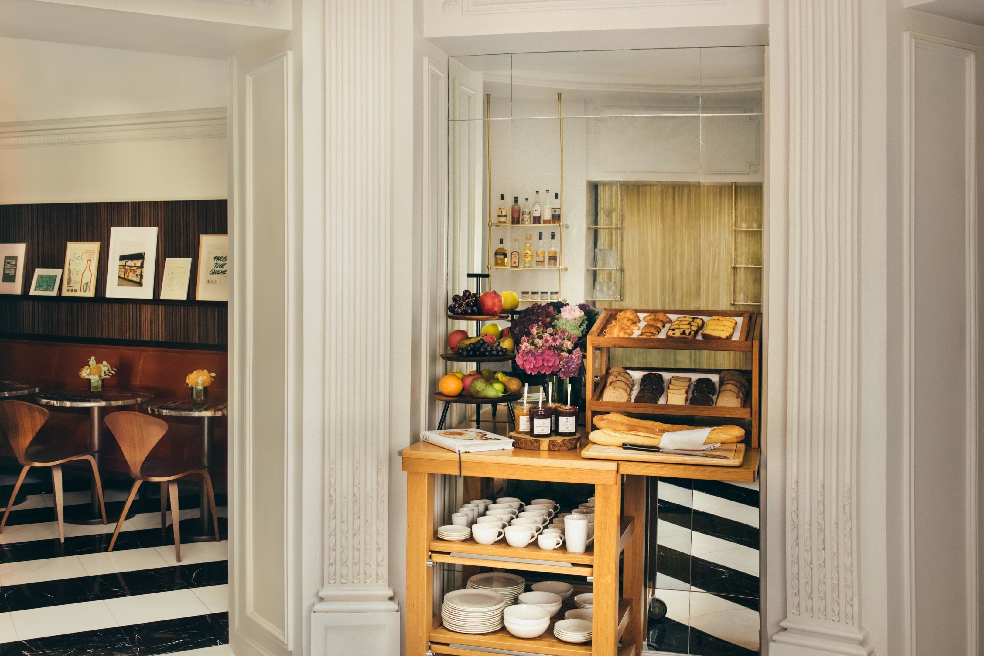 A dining area with a wooden table and chairs, a buffet counter with food and drinks, and a wall with framed pictures.