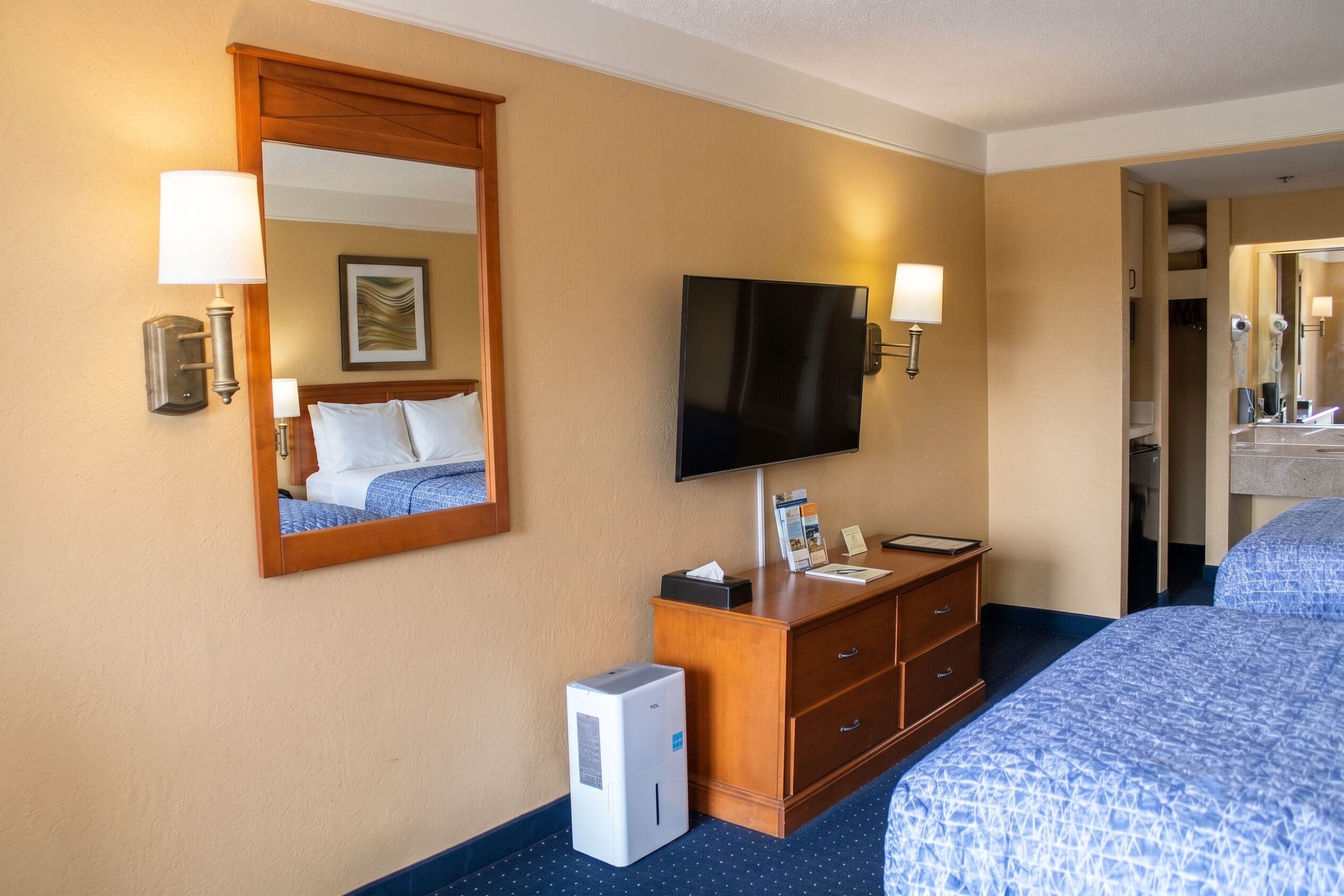 Une chambre d’hôtel équipée d’un lit, d’une commode, d’une télévision, d’un miroir et d’un petit climatiseur.