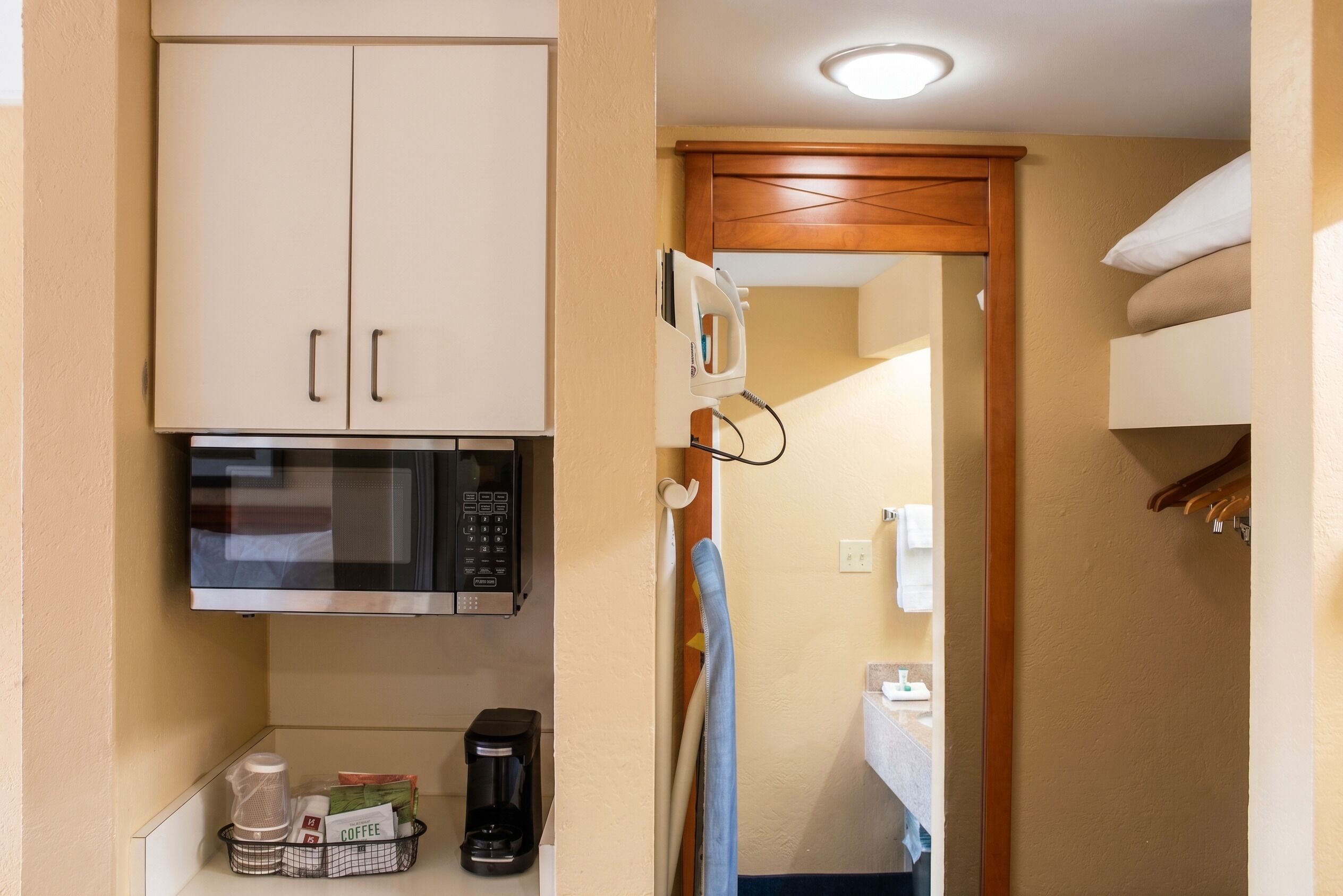 A compact kitchenette with a microwave, coffee maker, and storage for coffee pods.