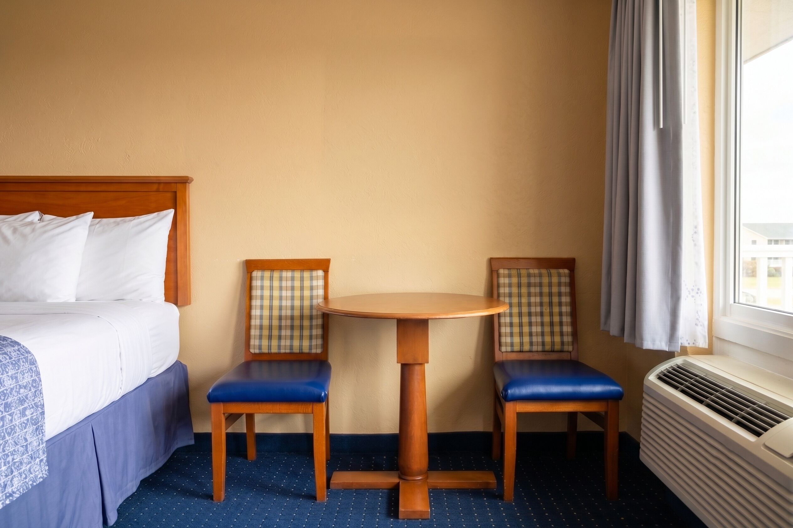 Una habitación de hotel con una cama, dos sillas, una mesita y una ventana con cortinas.