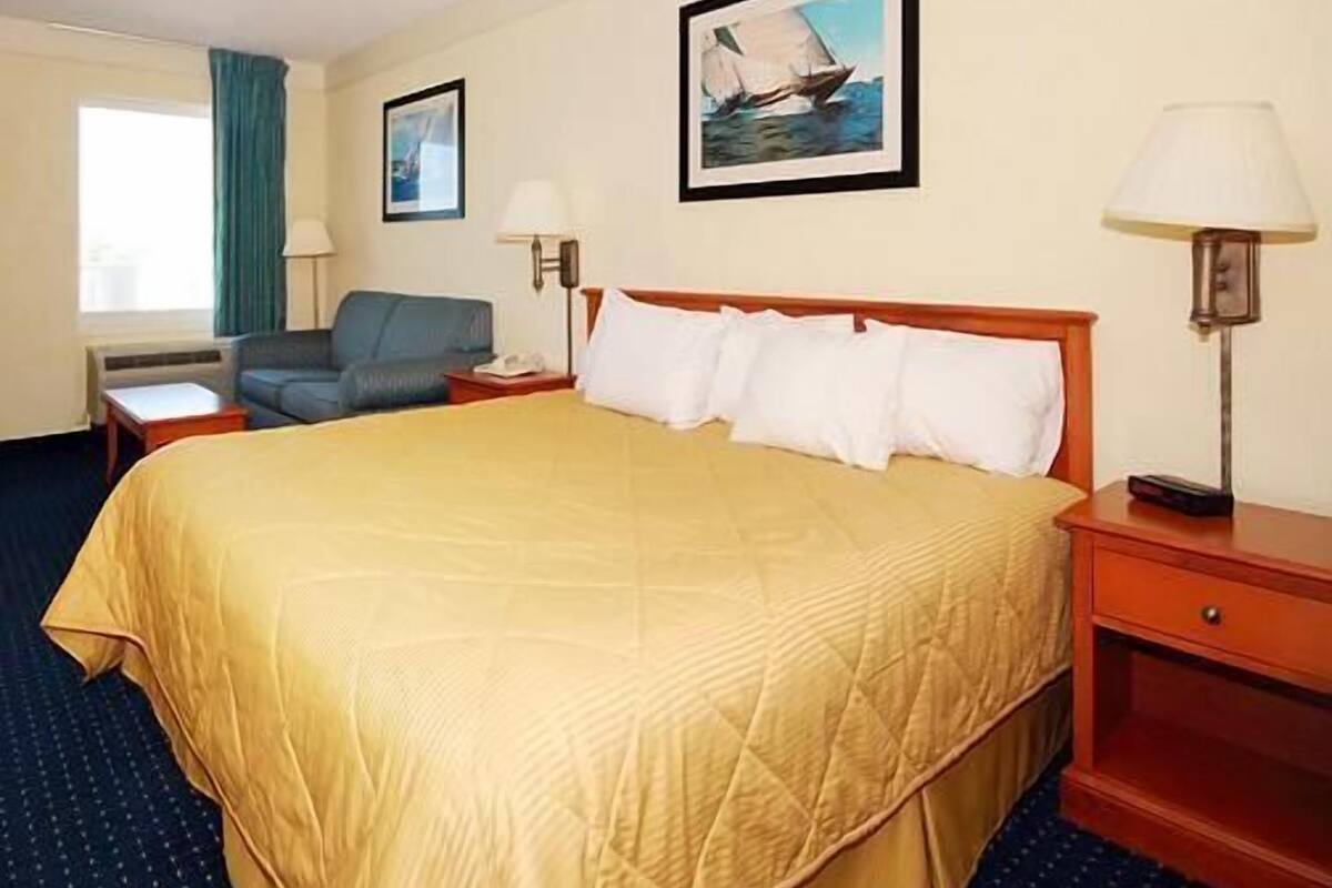 A hotel room with a large bed, a desk, a chair, a window with curtains, and a painting on the wall.