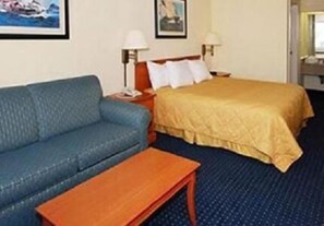 A hotel room with a blue sofa, a wooden nightstand, a bed with a yellow bedspread, and two wall-mounted lamps. - Hatteras Island Inn (Buxton)