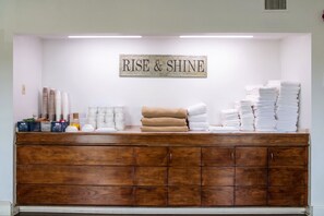 A reception area with a wooden cabinet, a sign that reads 'RISE & SHINE', and stacks of white towels.