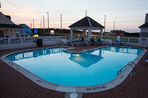 A swimming pool with lounge chairs and a gazebo, surrounded by a white fence and brick walkway. - Hatteras Island Inn (Buxton)