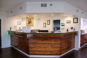 A reception desk with a wooden finish, a framed picture above it, and a sign indicating pet policies.