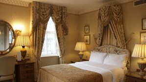 Ein klassisches Hotelzimmer mit einem großen Bett, zwei Nachttischen mit Lampen, einem Schreibtisch mit Stuhl und einem großen Spiegel.