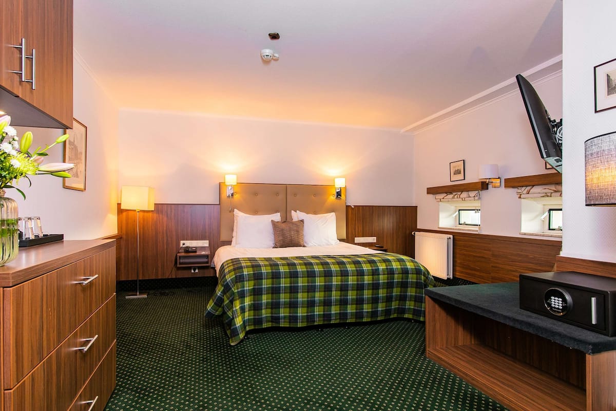A hotel room with a bed, bedside tables, a desk, and a safe.