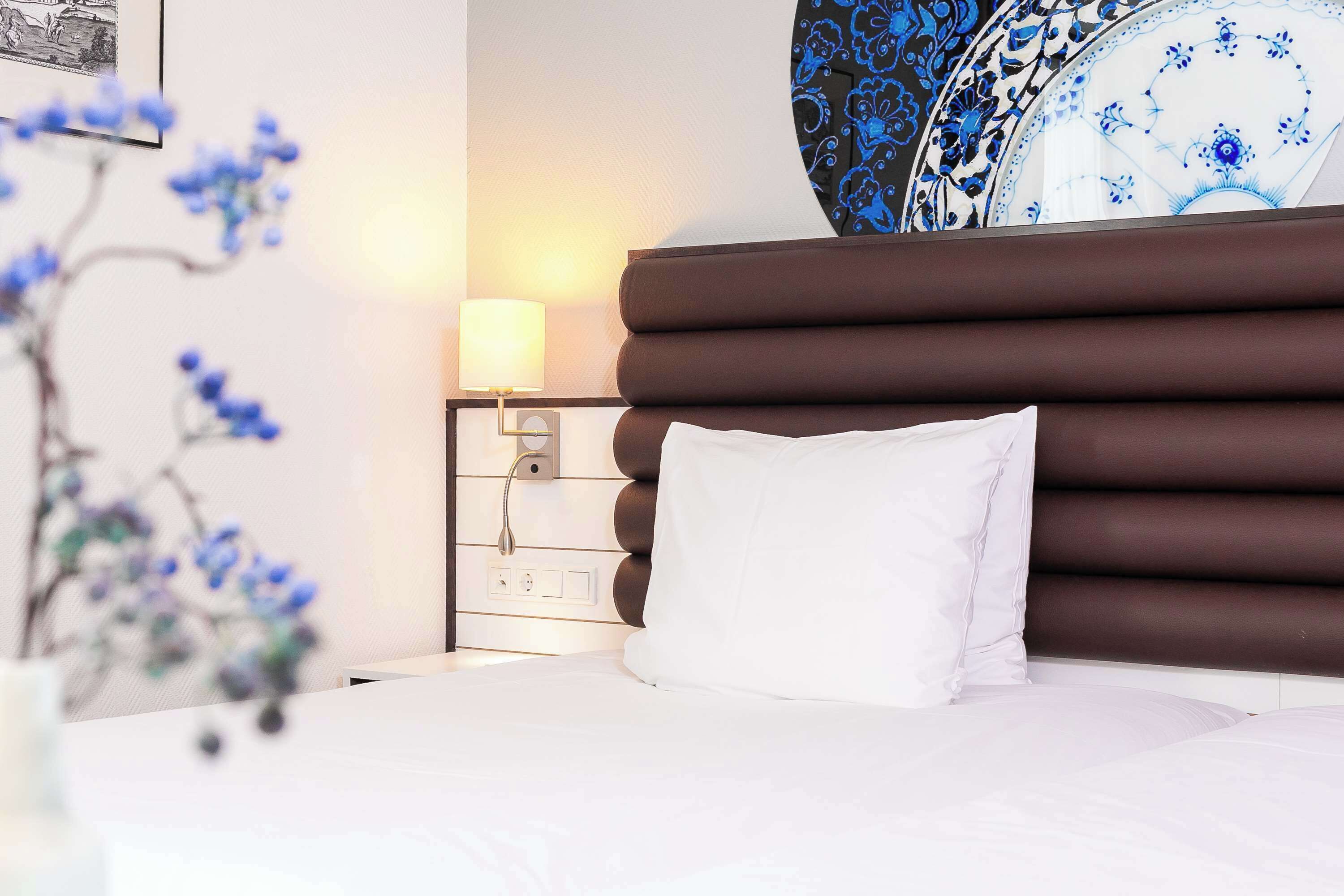 Un lit bien fait, avec un oreiller blanc, une table de chevet avec une lampe et une prise de courant fixée au mur.