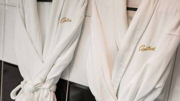 Two white robes with "Central" embroidered in gold, hanging on a rack in a bathroom.